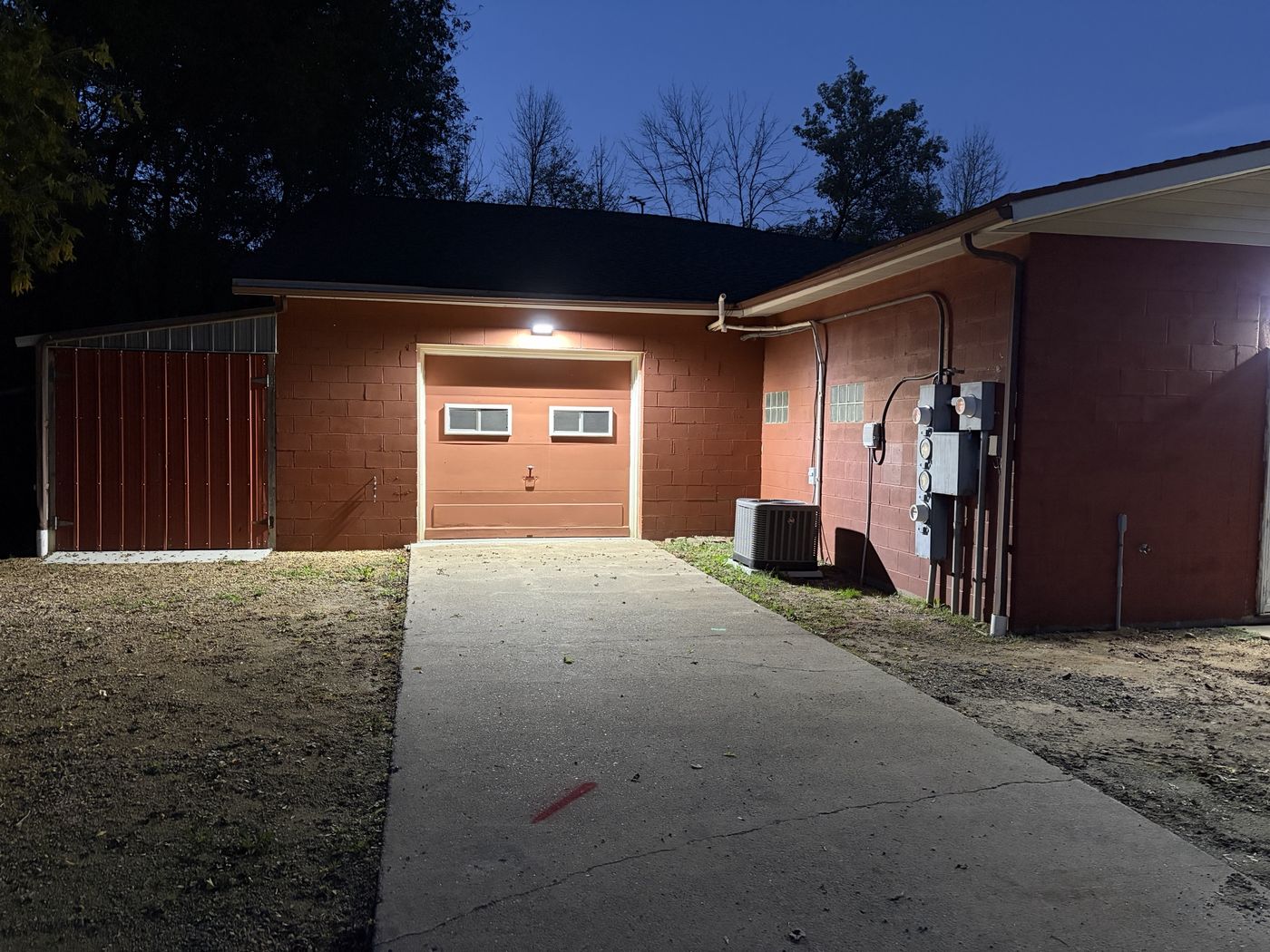 The Shop exterior at dusk — painted block wall and drive-in garage door with new wall lighting
