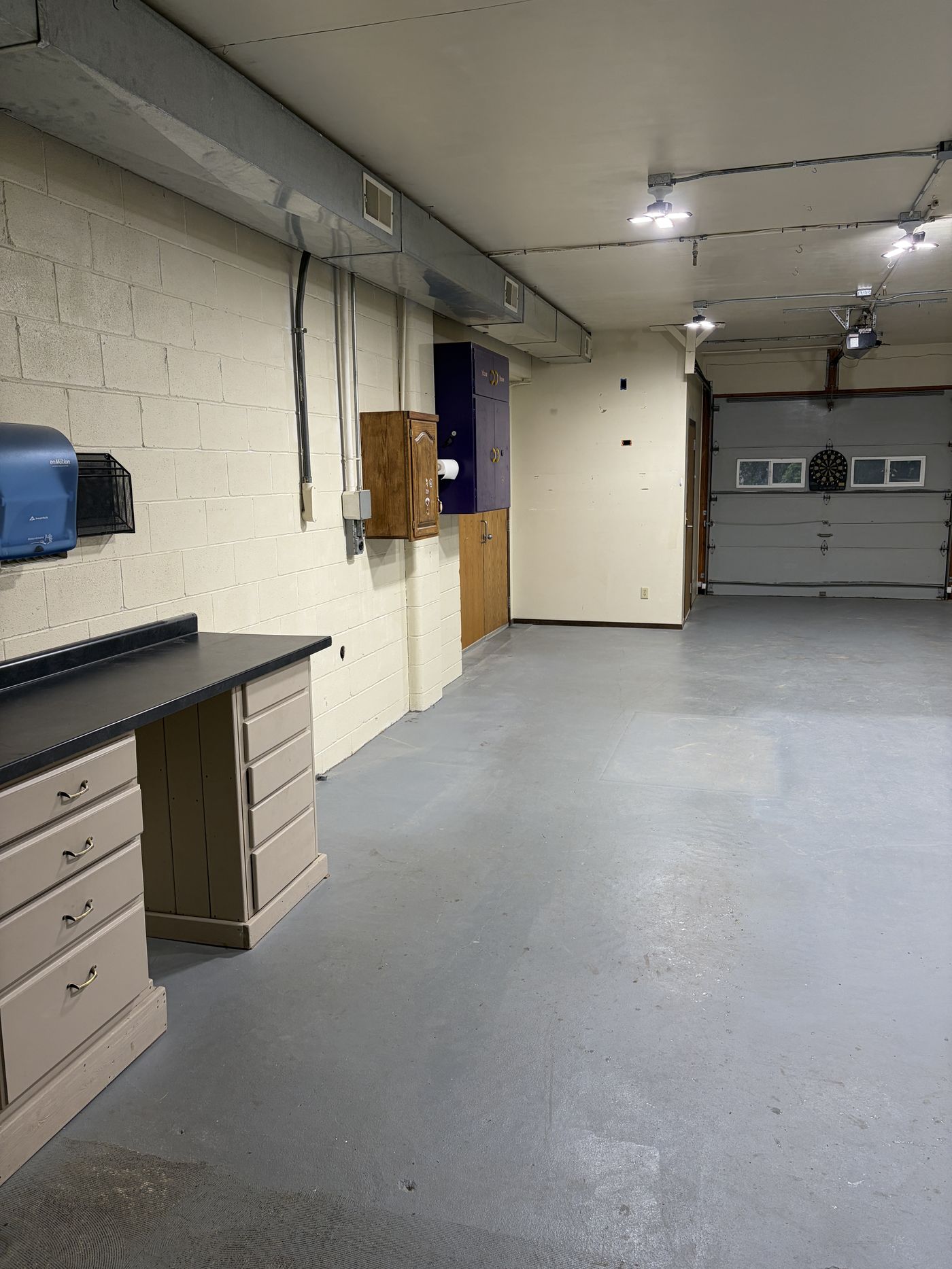 The Shop interior — open gray floor, built-in counter and cabinets, overhead lighting, drive-in garage door at the back